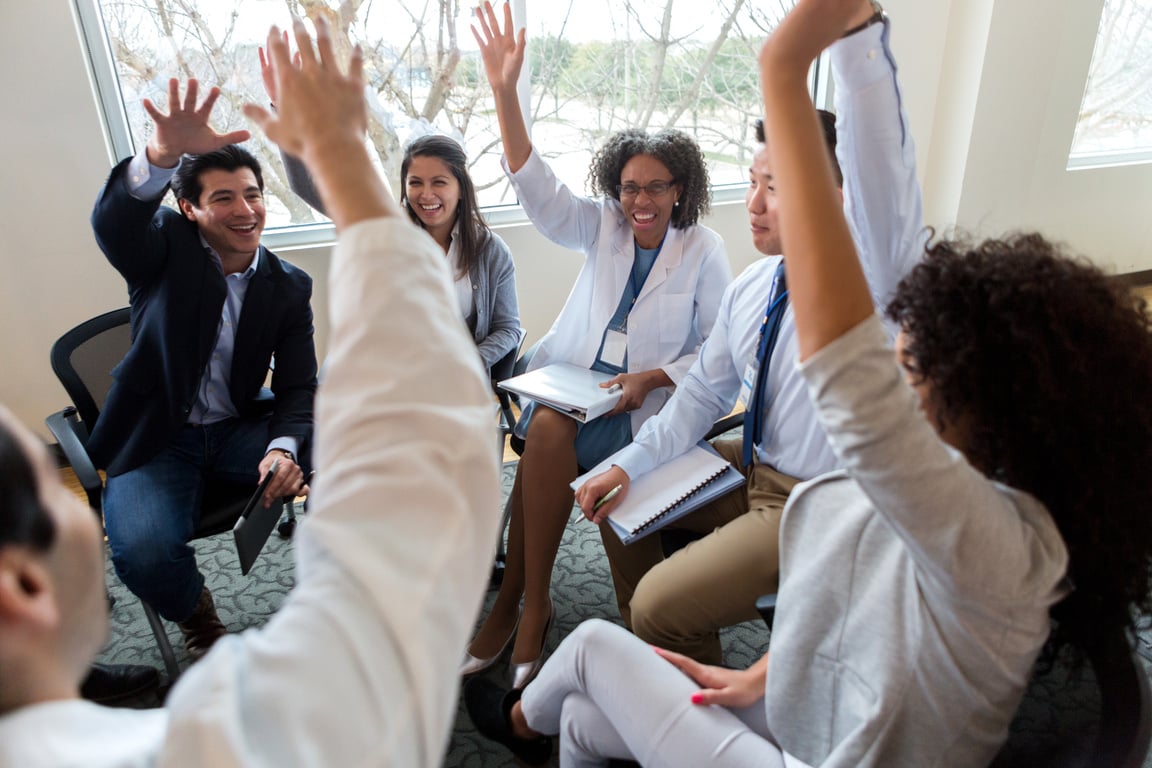 Employees all raise hands during medical staff meeting